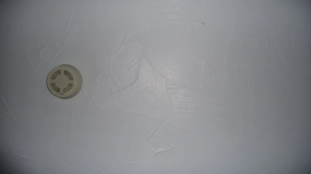 A smoke detector mounted high on a white ceiling